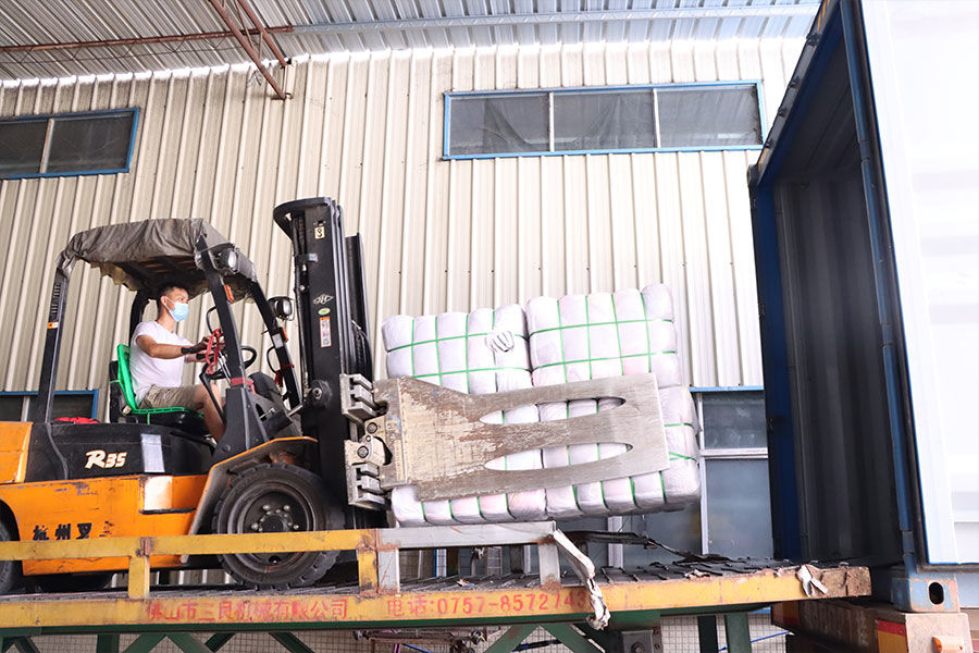 forklift operator carrying several bales of used shoes in a cargo container
