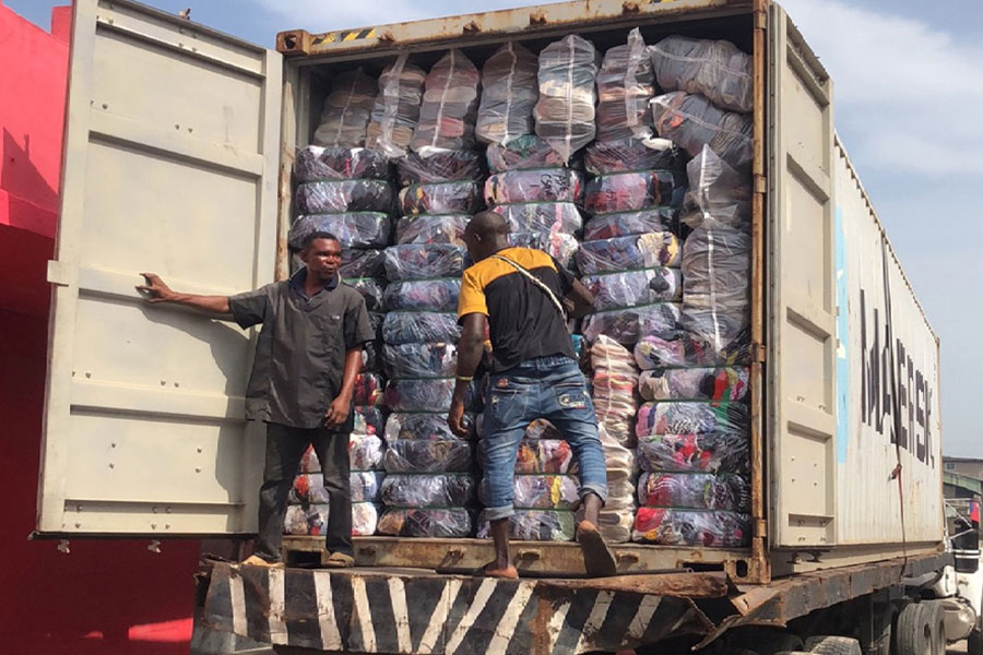 employees inspecting the cargo container loaded with bales of used shoes